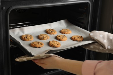 Woman taking out delicious chocolate chip cookies from oven, closeup