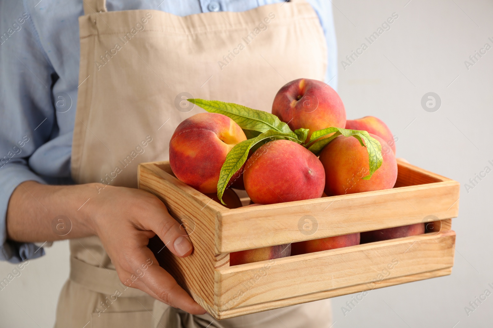 Photo of Woman with fresh sweet peaches in wooden crate, closeup