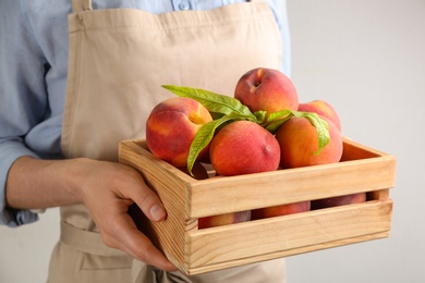 Woman with fresh sweet peaches in wooden crate, closeup