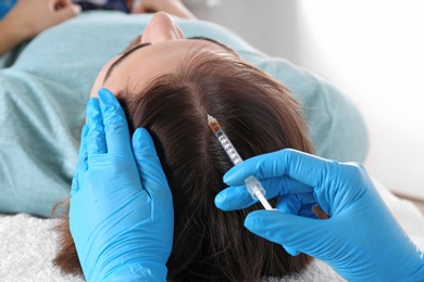 Young man with hair loss problem receiving injection in salon, closeup