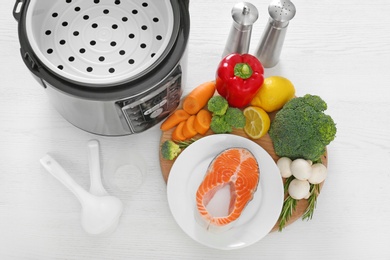 Modern multi cooker and products on white wooden table, above view
