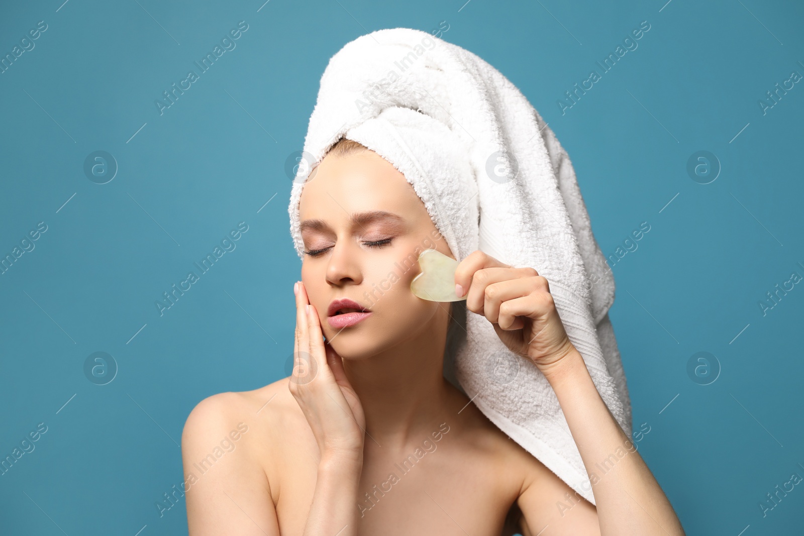 Photo of Beautiful young woman doing facial massage with gua sha tool on blue background