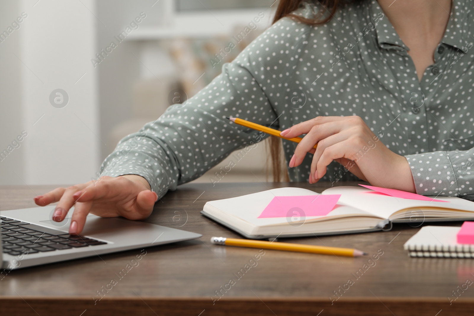 Photo of Woman with notebook working on laptop at wooden table indoors, closeup