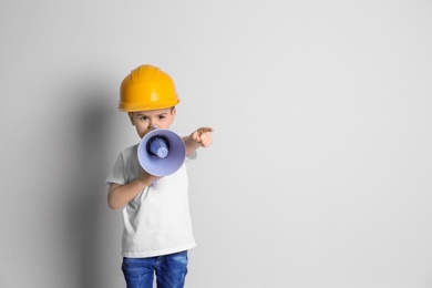 Photo of Adorable little boy in hardhat with megaphone on light background