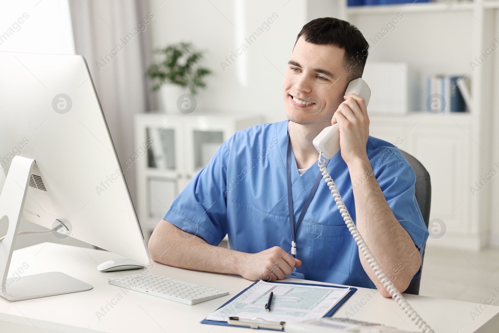 Photo of Smiling medical assistant talking by phone in office