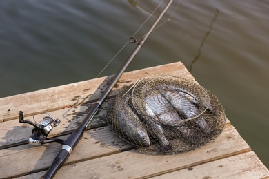 Photo of Fishing rod and fresh fish on wooden pier near pond