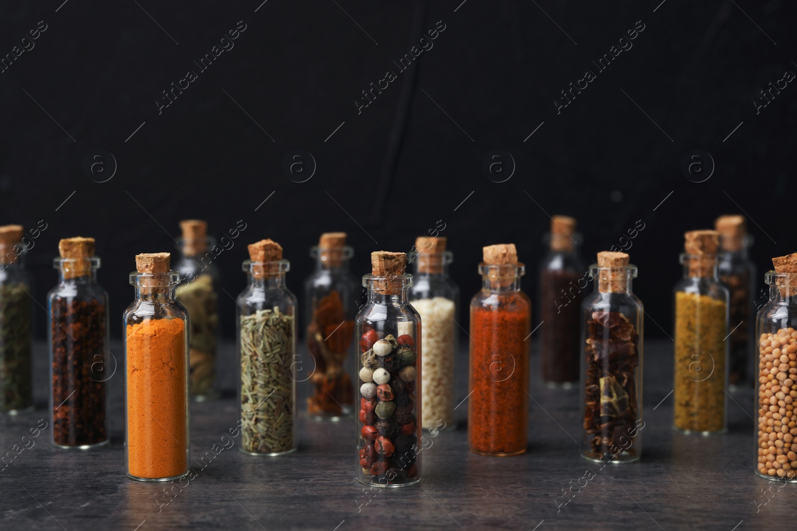 Photo of Glass bottles with different spices on table against black background