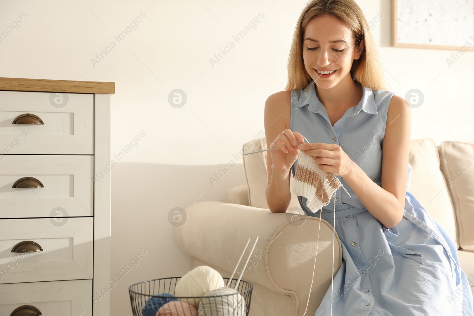 Photo of Young woman knitting with needles on sofa at home. Handicraft as hobby