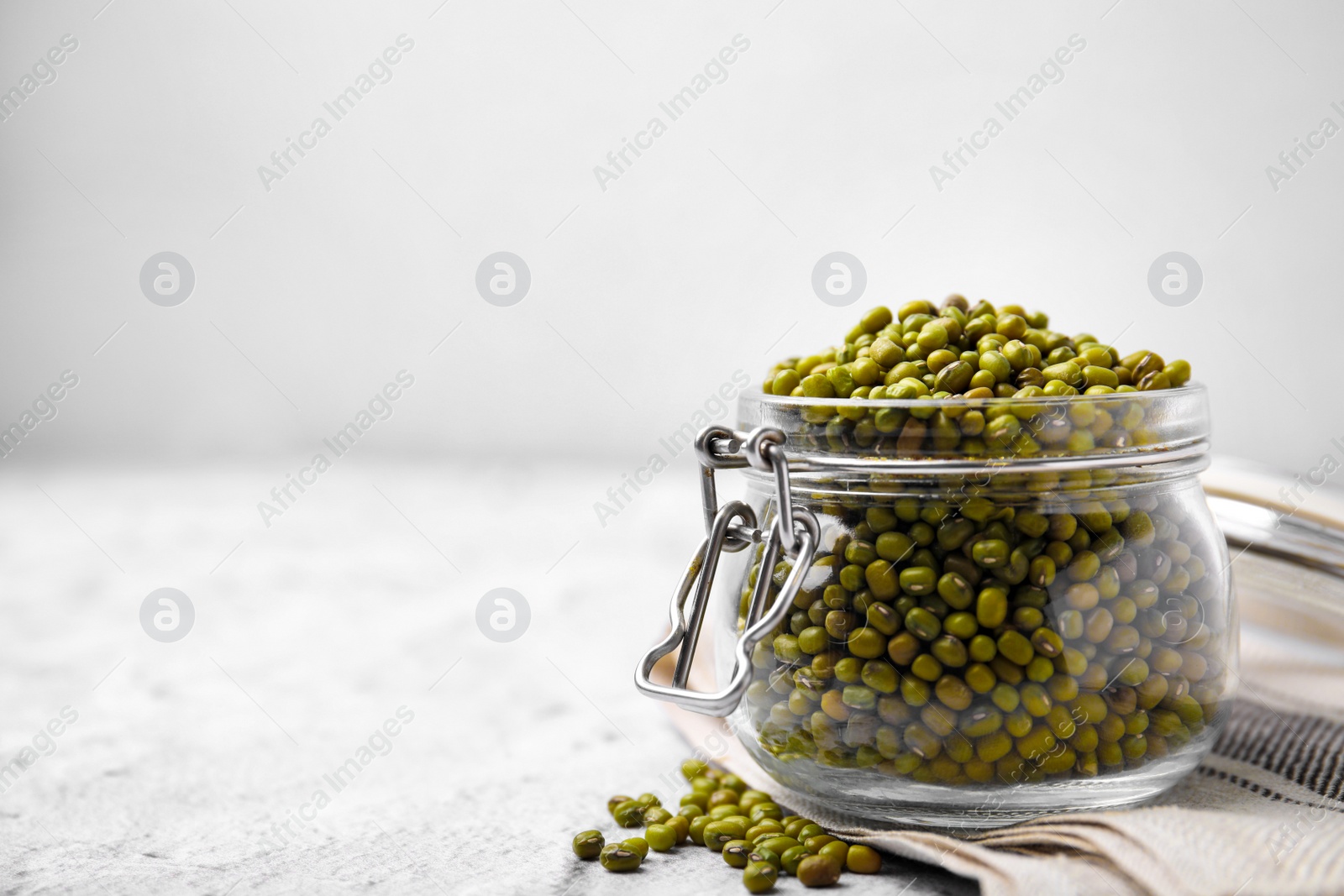 Photo of Glass jar with green mung beans on white textured table, closeup. Space for text