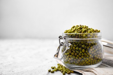 Photo of Glass jar with green mung beans on white textured table, closeup. Space for text