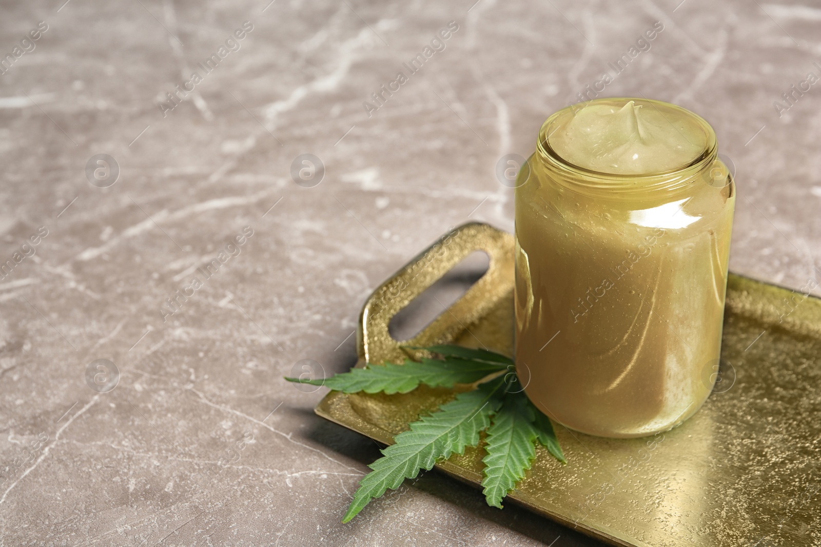 Photo of Tray with jar of hemp lotion and fresh leaf on gray table. Space for text