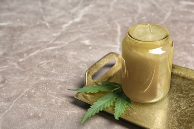 Photo of Tray with jar of hemp lotion and fresh leaf on gray table. Space for text