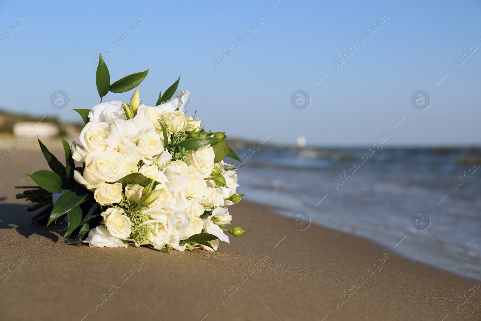 Photo of Beautiful wedding bouquet on sandy beach near sea. Space for text