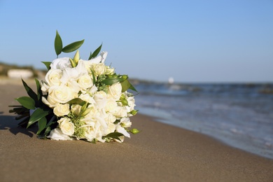 Beautiful wedding bouquet on sandy beach near sea. Space for text