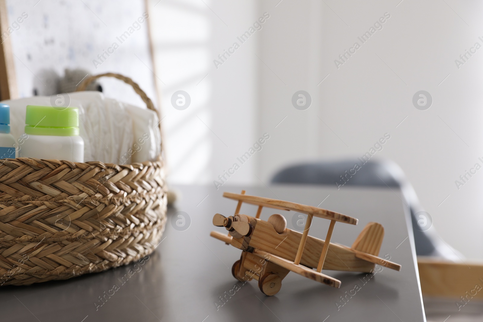 Photo of Wicker basket with accessories and wooden airplane on grey table in child room