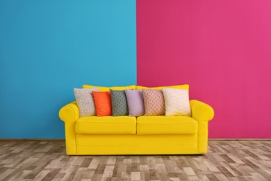 Sofa with different pillows near color wall in room