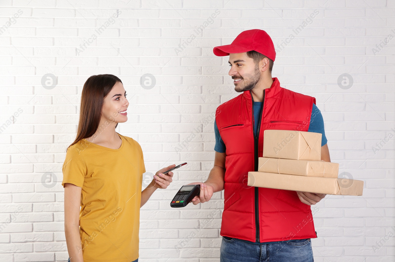 Photo of Young woman with smartphone using terminal for delivery payment against brick wall