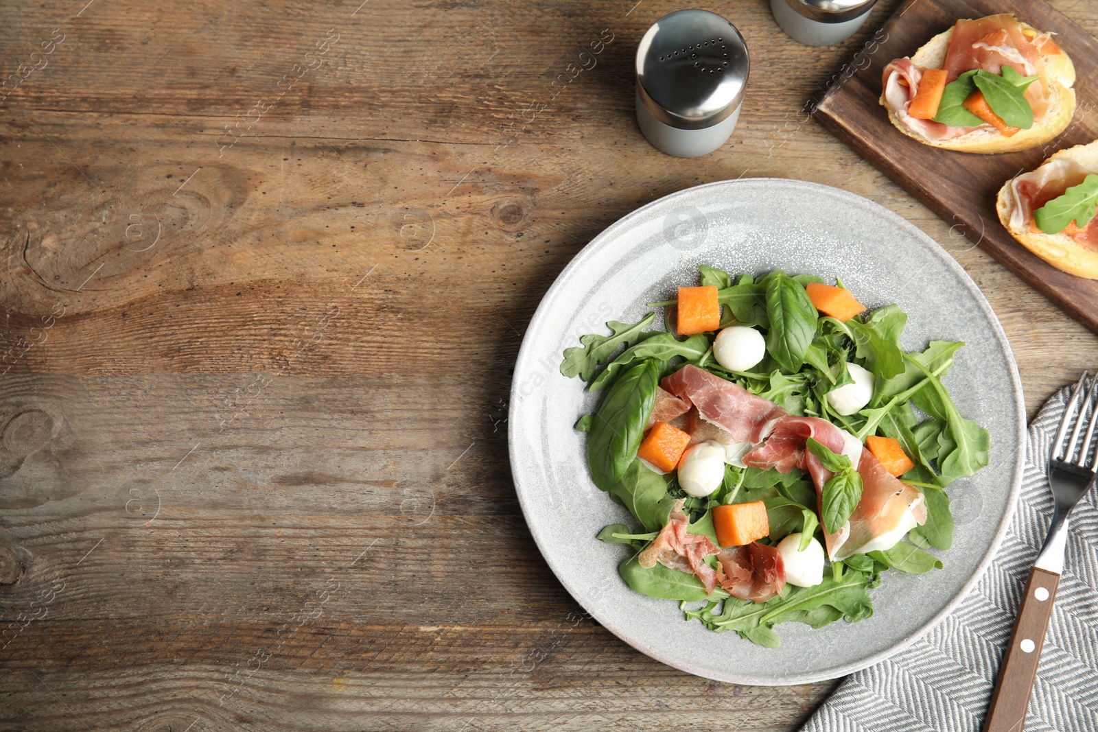 Photo of Flat lay composition of fresh melon with prosciutto on wooden table. Space for text