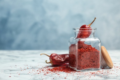 Jar with crushed chili pepper and pods on table