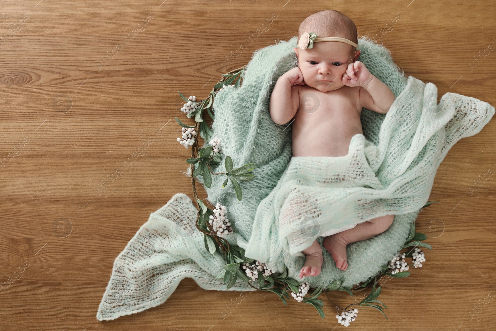 Photo of Adorable little baby with green blanket and floral decor on wooden background, top view. Space for text