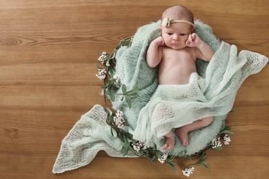 Photo of Adorable little baby with green blanket and floral decor on wooden background, top view. Space for text