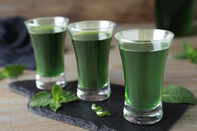 Delicious mint liqueur with green leaves on wooden table, closeup