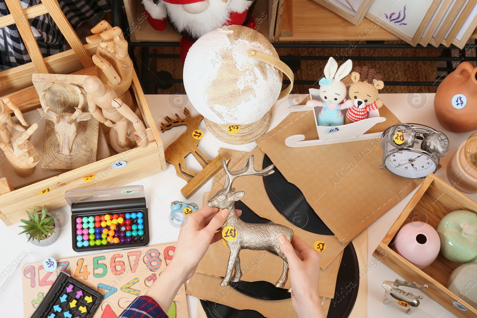 Photo of Woman holding toy deer near table with many different stuff, above view. Garage sale