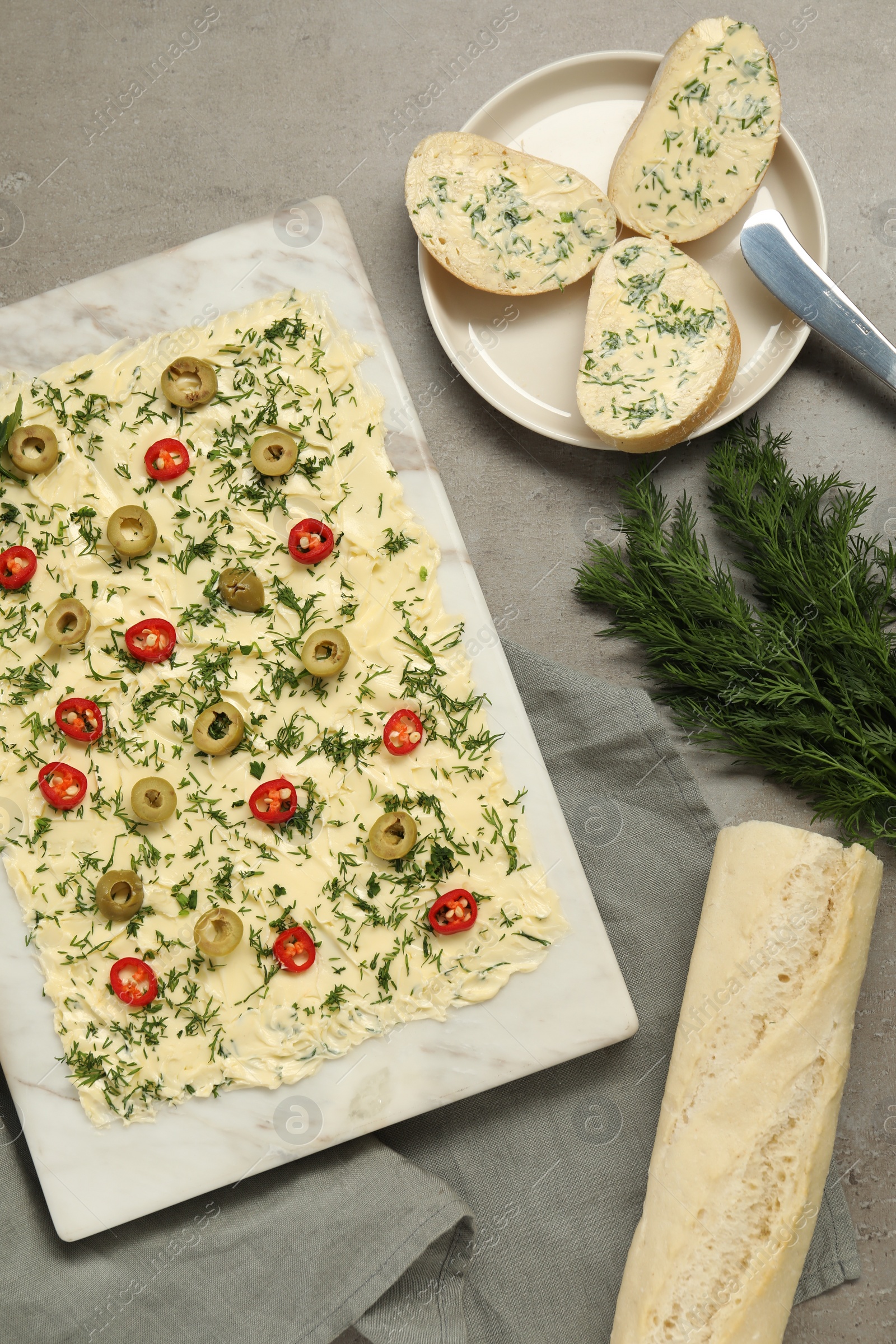 Photo of Fresh butter board with cut olives, dill and bread on grey table, flat lay