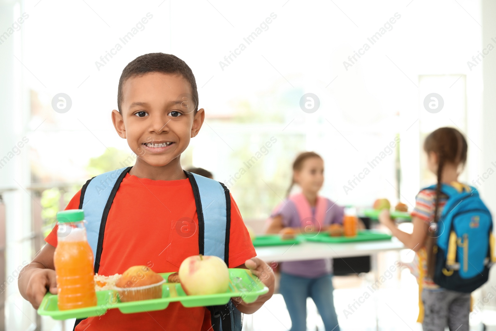 Photo of African-American boy holding tray with healthy food at school canteen