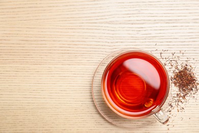 Freshly brewed rooibos tea and scattered dry leaves on wooden table, flat lay. Space for text