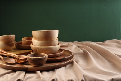 Set of wooden dishware and utensils on table against green background. Space for text