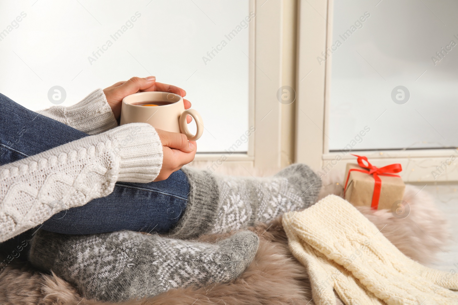 Photo of Woman with cup of hot mulled wine sitting on window sill, closeup. Winter drink