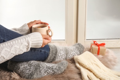 Photo of Woman with cup of hot mulled wine sitting on window sill, closeup. Winter drink