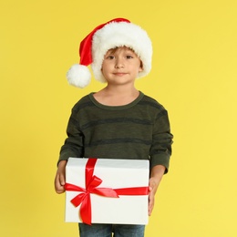 Photo of Cute little boy in Santa hat with Christmas gift on yellow background