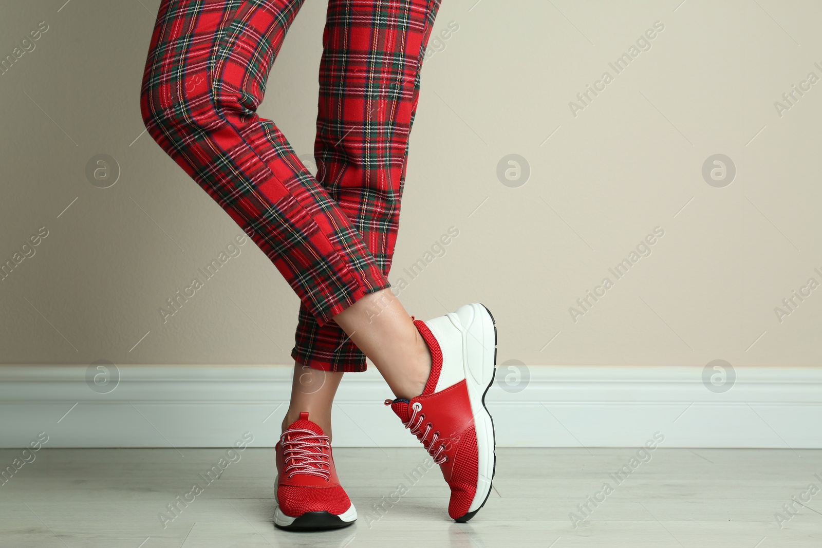 Photo of Woman wearing stylish sneakers near beige wall indoors, closeup