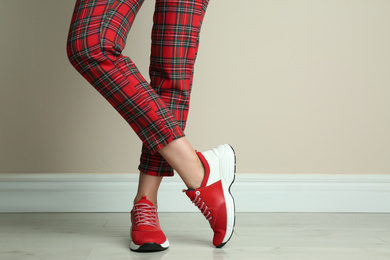 Photo of Woman wearing stylish sneakers near beige wall indoors, closeup