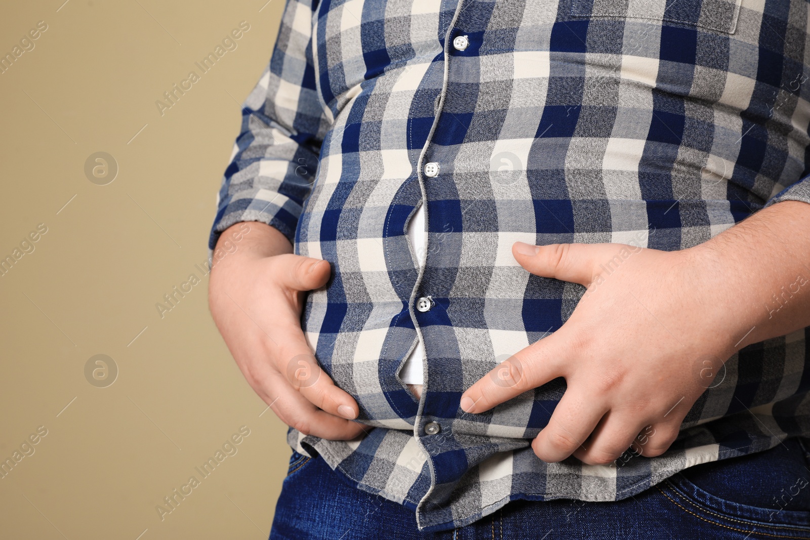 Photo of Overweight man in tight shirt on beige background, closeup