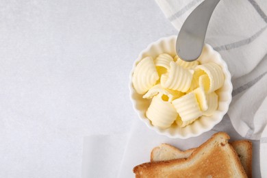 Photo of Tasty butter curls in bowl, knife and toasts on light grey table, top view. Space for text
