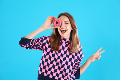 Beautiful young woman with donut on light blue background