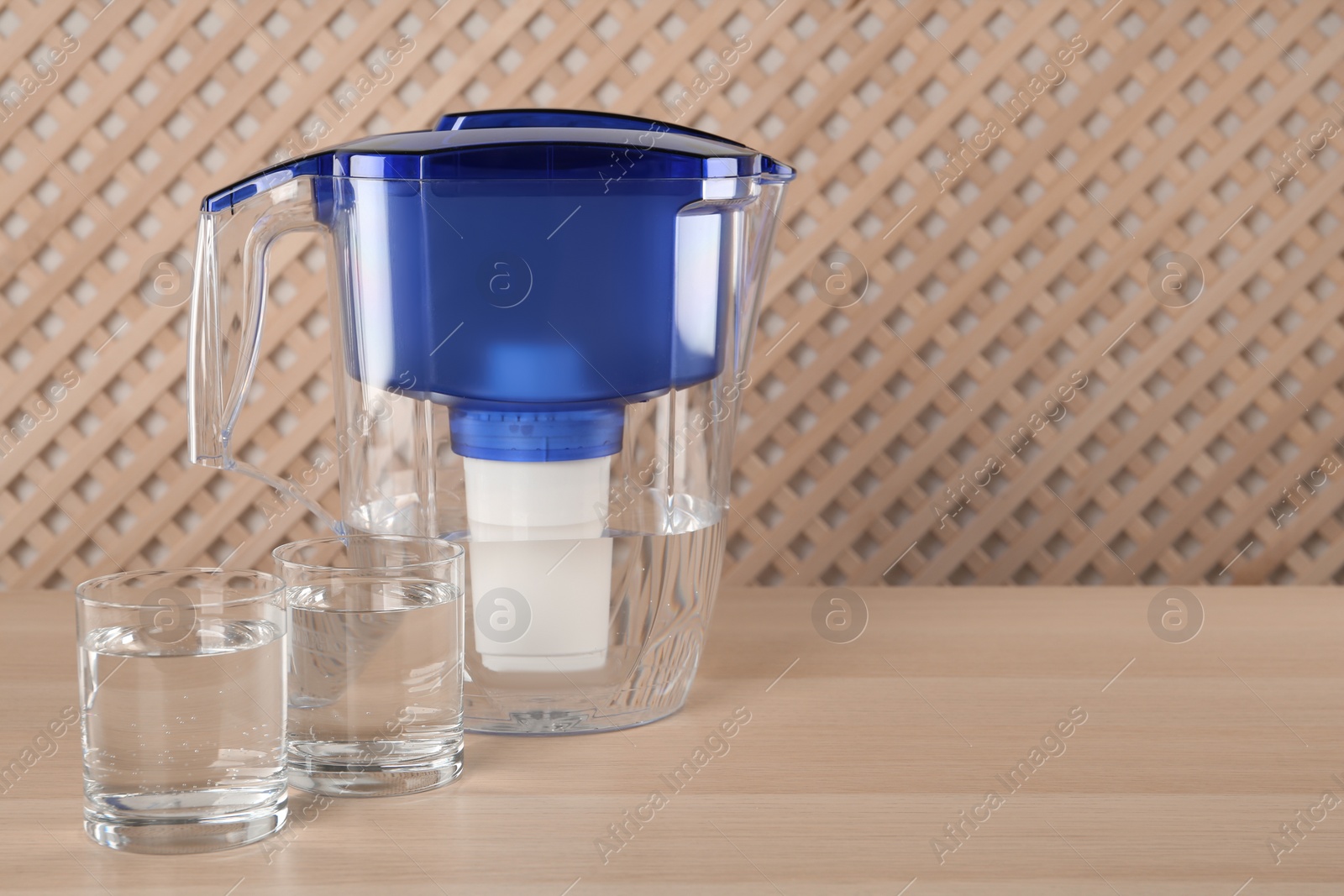 Photo of Filter jug and glasses with purified water on wooden table indoors. Space for text