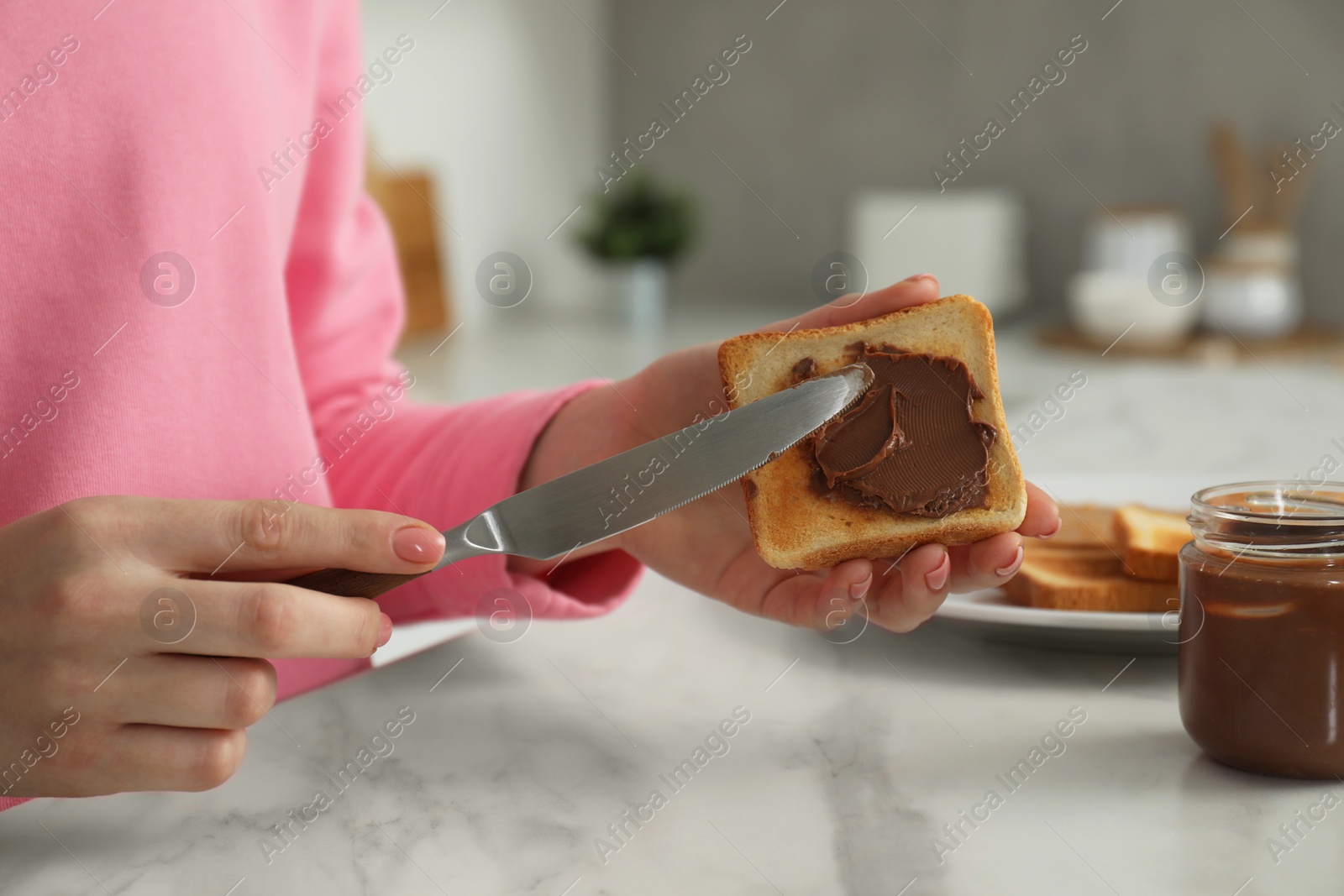 Photo of Woman spreading tasty nut butter onto toast at white marble table, closeup