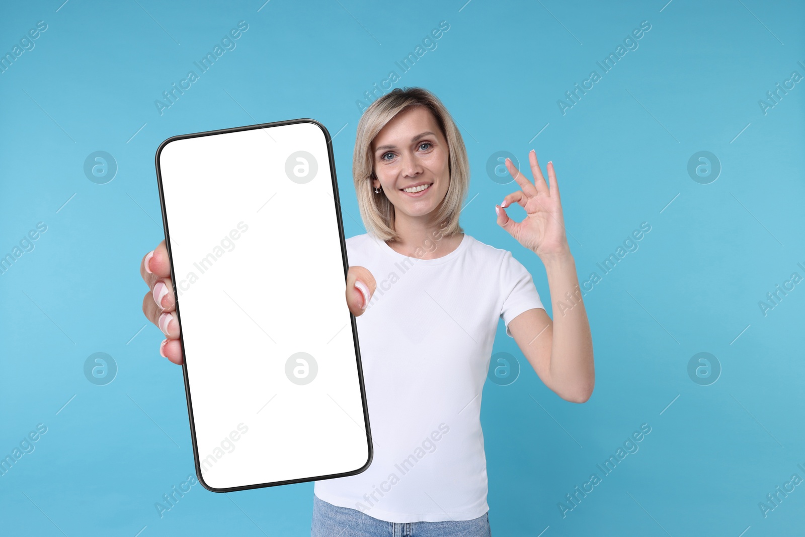 Image of Happy woman showing mobile phone with blank screen on light blue background. Mockup for design