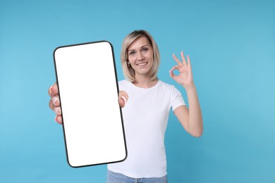 Happy woman showing mobile phone with blank screen on light blue background. Mockup for design