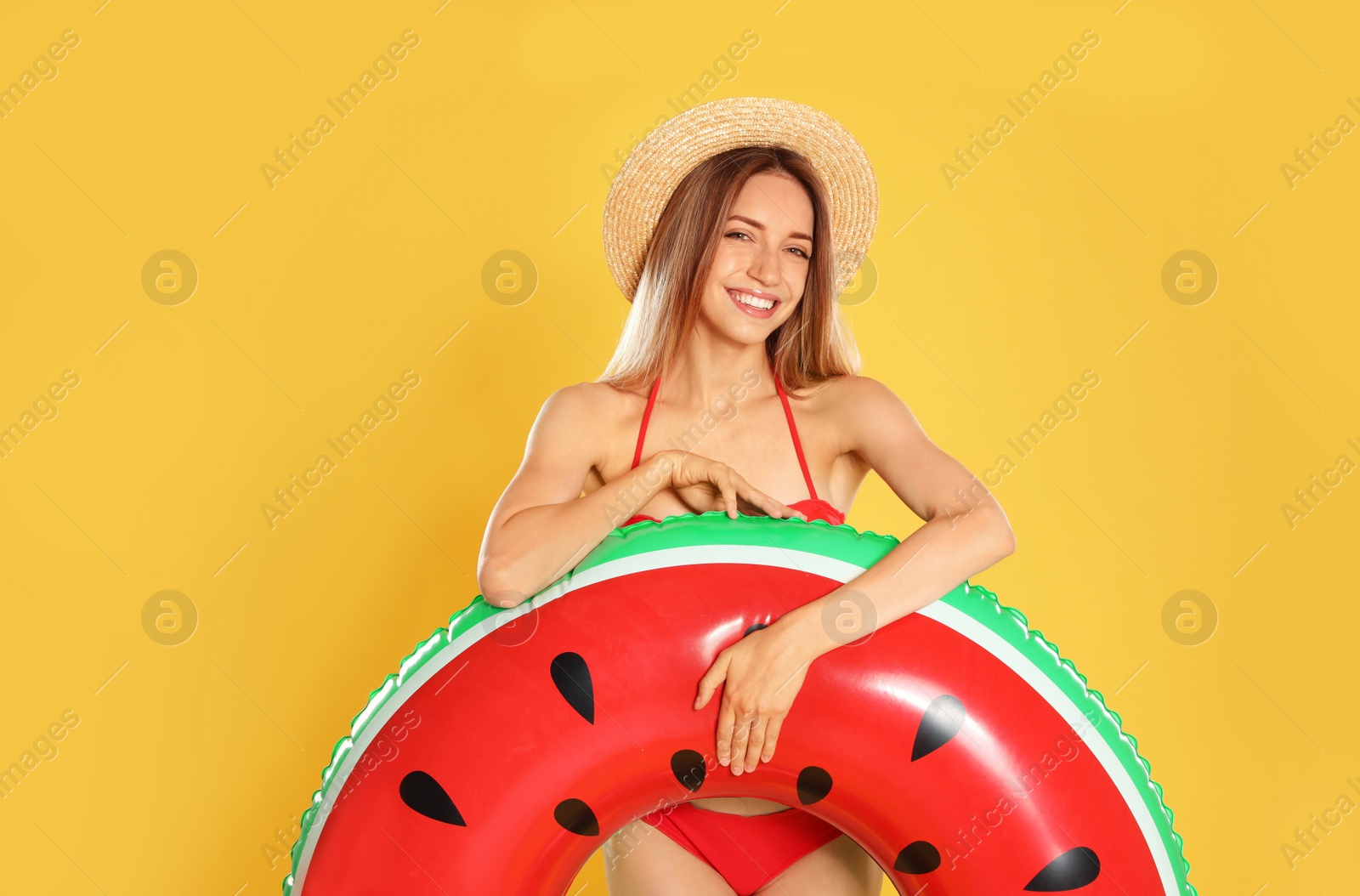 Photo of Beautiful young woman in stylish bikini with watermelon inflatable ring on yellow background