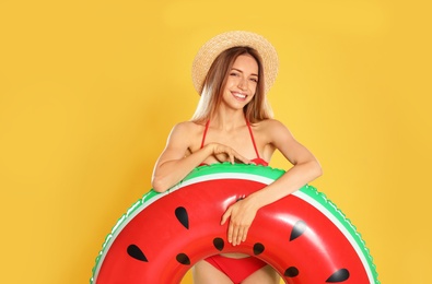 Photo of Beautiful young woman in stylish bikini with watermelon inflatable ring on yellow background
