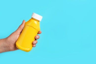 Photo of Woman with bottle of mustard on light blue background, closeup. Space for text
