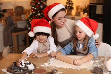 Mother with her cute little children making dough for Christmas cookies in kitchen