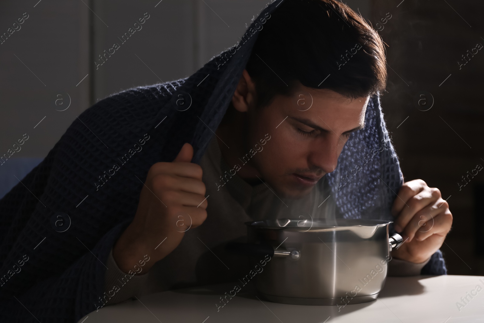 Photo of Man with plaid doing inhalation above saucepot at table indoors