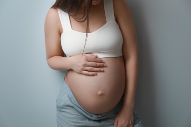 Pregnant young woman touching belly on grey background, closeup
