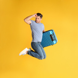 Photo of Handsome man with suitcase for summer trip jumping on yellow background. Vacation travel